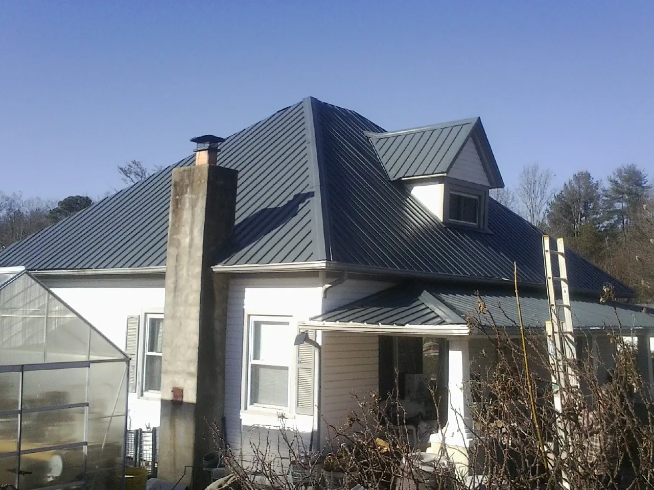 Dark blue standing seam metal roof on a white farmhouse with dormer — Slate & Tile Roof Repair by Roofing Brothers in Greenview