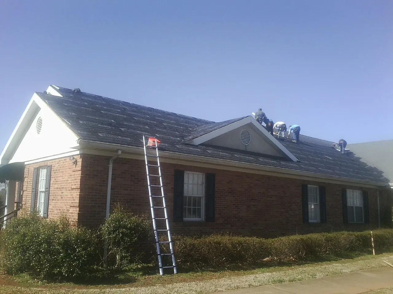 Crew tearing shingles off a brick ranch roof with a ladder set — Metal Roof Repair work by our crew in Greenview