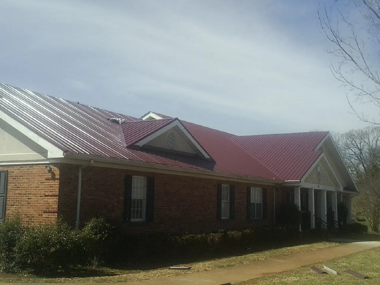 Red metal roof with gabled entries on a long brick building, from a Hail Damage Roof Repair job in Greenview