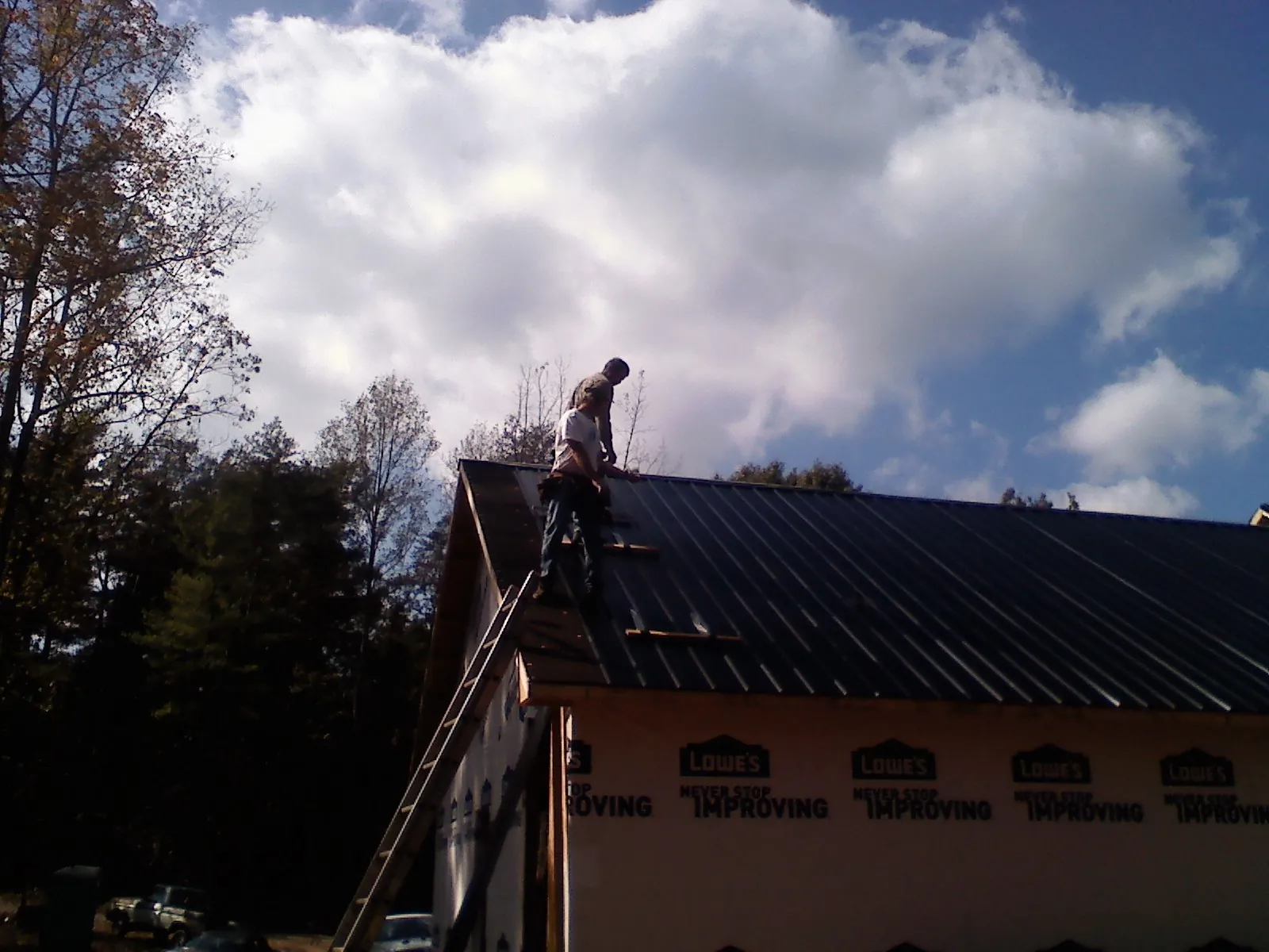 Roofer fastening dark metal panels high against a cloudy sky, from a Roof Inspection job in Greenview